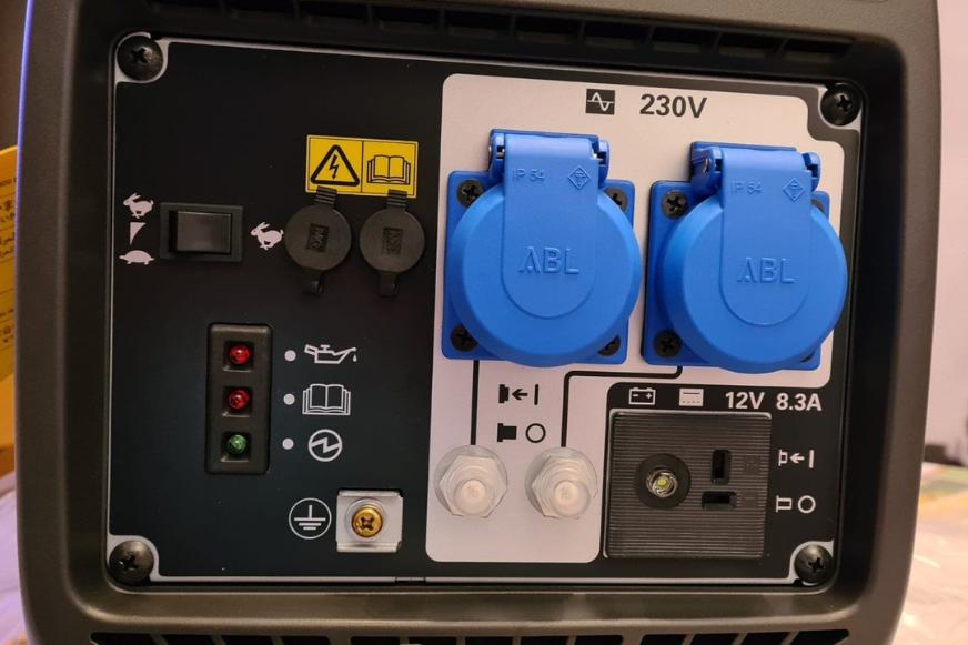 Der Honda EU 22i Notstromaggregat steht auf dem Boden und die 2 Schukostecker und die Warnleuchten sowie Bedienungs-Tasten sind zu sehen.